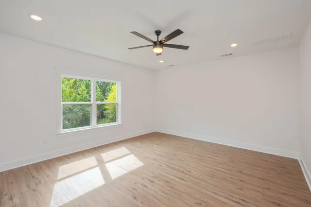 an empty room with wooden floor a ceiling fan and windows
