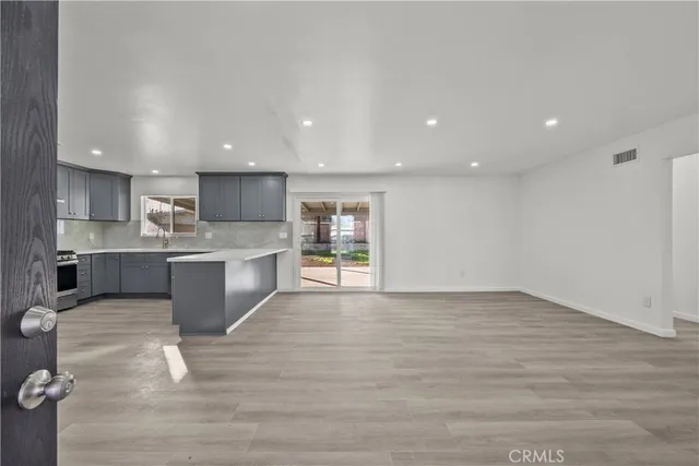 a view of an empty room with wooden floor and a kitchen