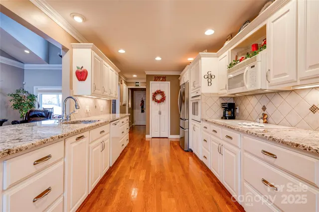 a large kitchen with stainless steel appliances kitchen island granite countertop a large counter top space a sink white cabinets and wooden floor