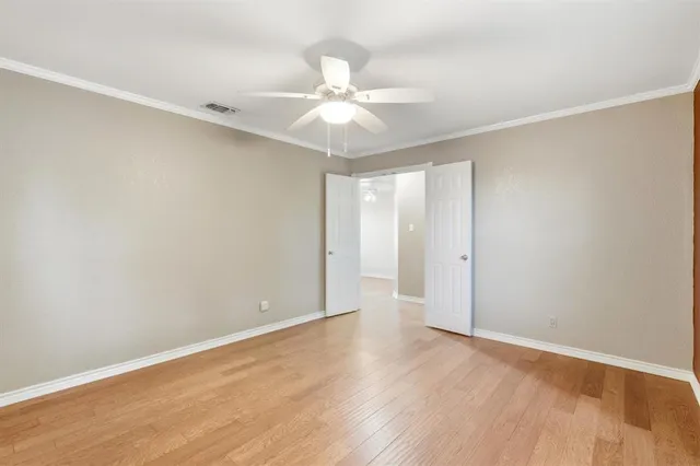 a view of an empty room with wooden floor and a ceiling fan