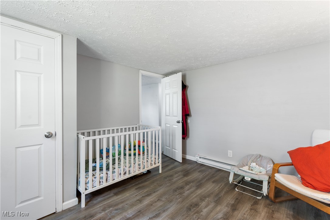 271 Sterling Avenue Rittman, OH 44270 - Photo 22 of 31 Bedroom with wood finished floors, a textured ceiling, baseboards, a crib, and baseboard heating