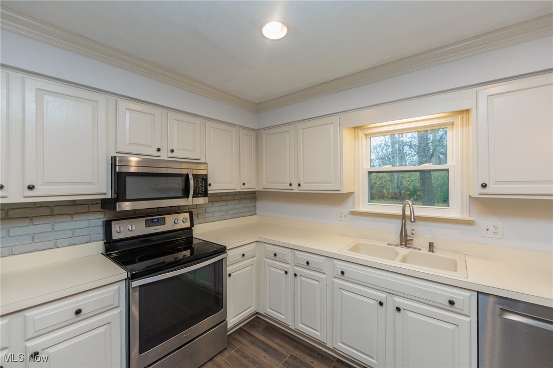 28013 Knickerbocker Road Bay Village, OH 44140 - Photo 10 of 38 Kitchen featuring stainless steel appliances, light countertops, wood finish floors, white cabinets, and crown molding