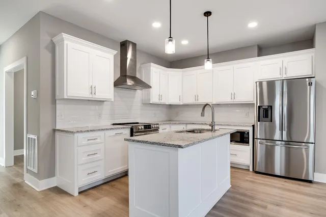 a kitchen with stainless steel appliances granite countertop a refrigerator a stove a sink and white cabinets with wooden floor