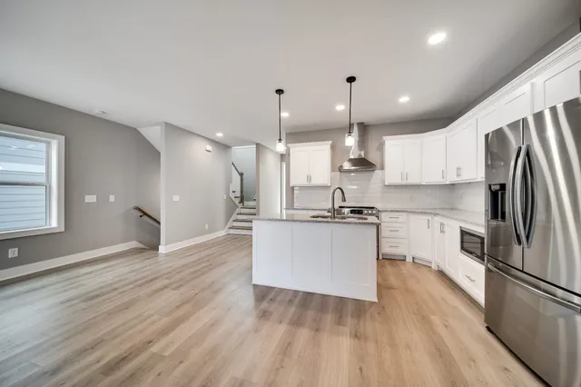 a kitchen with stainless steel appliances granite countertop a refrigerator a sink dishwasher a stove and white countertops with wooden floor