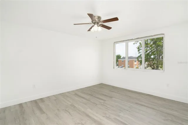 an empty room with wooden floor fan and windows