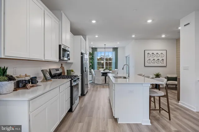 a large white kitchen with stainless steel appliances granite countertop a stove a sink a refrigerator white cabinets and wooden floor