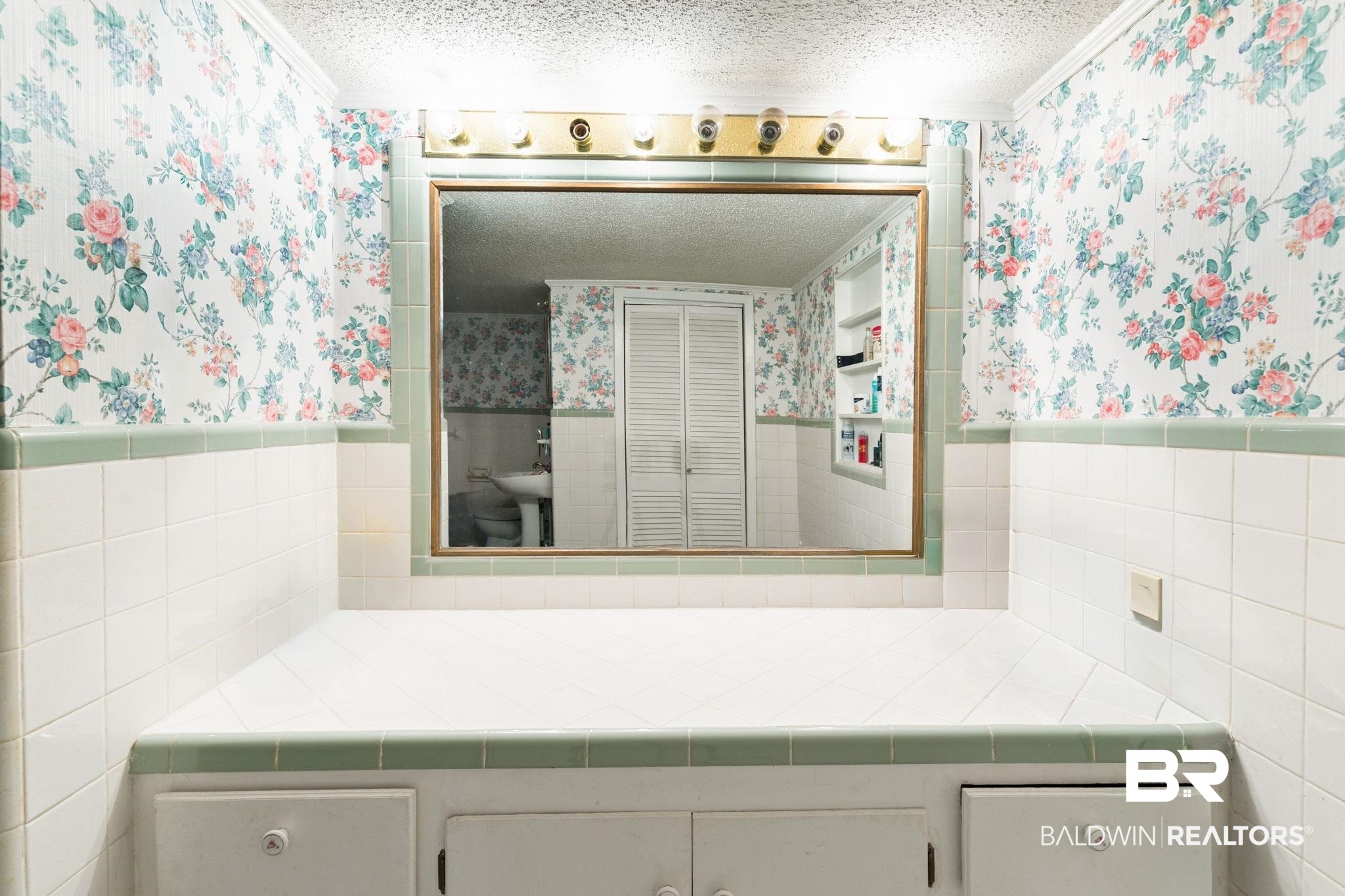 927 Cleveland Road Saraland, AL 36571 - Photo 22 of 80 Vanity area featuring a wall-mounted mirror with an integrated light fixture, a tile countertop, and cabinetry with white knob hardware