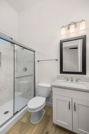 a bathroom with a toilet a sink a glass door a shower a mirror and vanity