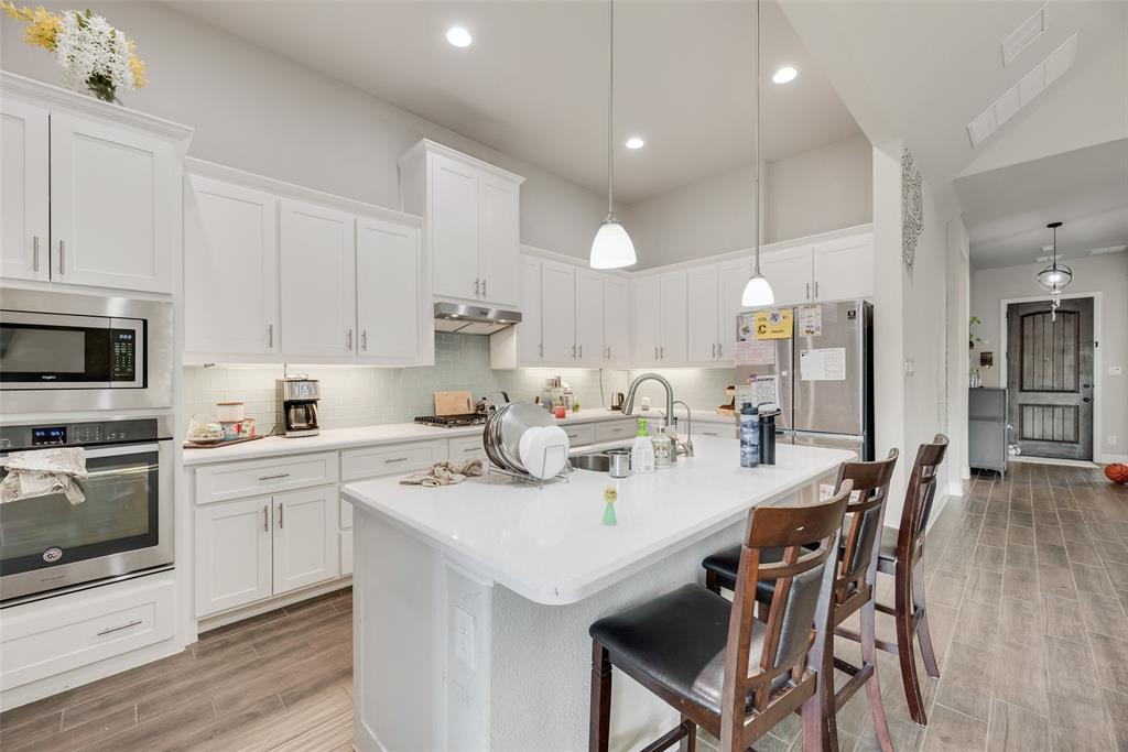14809 Cedar Flt Way Fort Worth, TX 76262 - Photo 5 of 18 Kitchen featuring appliances with stainless steel finishes, a kitchen bar, white cabinets, wood tiled floors, and an island with sink