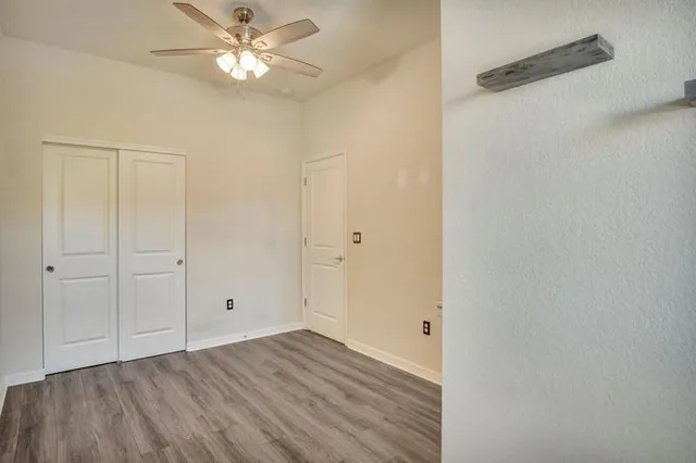 a view of an empty room with chandelier fan and wooden floor