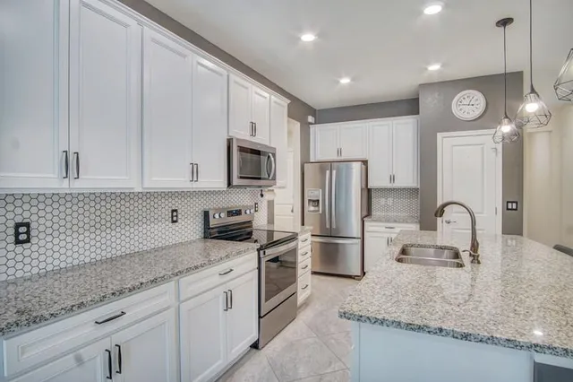 a kitchen with stainless steel appliances granite countertop a sink a stove a refrigerator a microwave oven with white cabinets and wooden floor