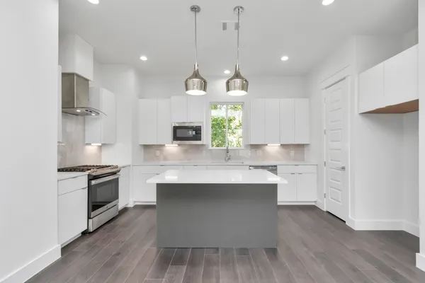 a kitchen with stainless steel appliances a stove a sink dishwasher a refrigerator white cabinets and wooden floor next to a window