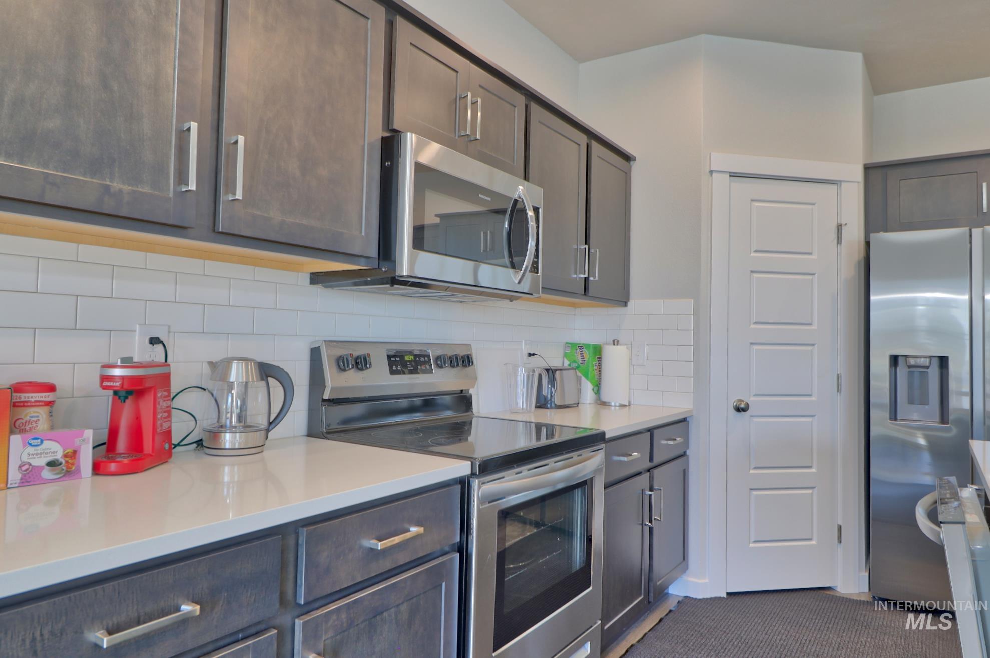 3508 South Edge Rim Way Meridian, ID 83642 - Photo 11 of 28 Kitchen featuring dark wood-finish cabinetry, stainless steel appliances, a subway tile backsplash, and light-toned countertops
