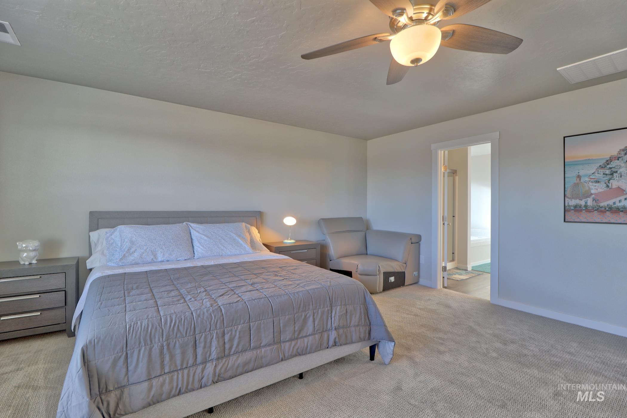 3508 South Edge Rim Way Meridian, ID 83642 - Photo 19 of 28 Carpeted bedroom with a ceiling fan light fixture, light-toned walls, and a doorway revealing a bathroom with a tub