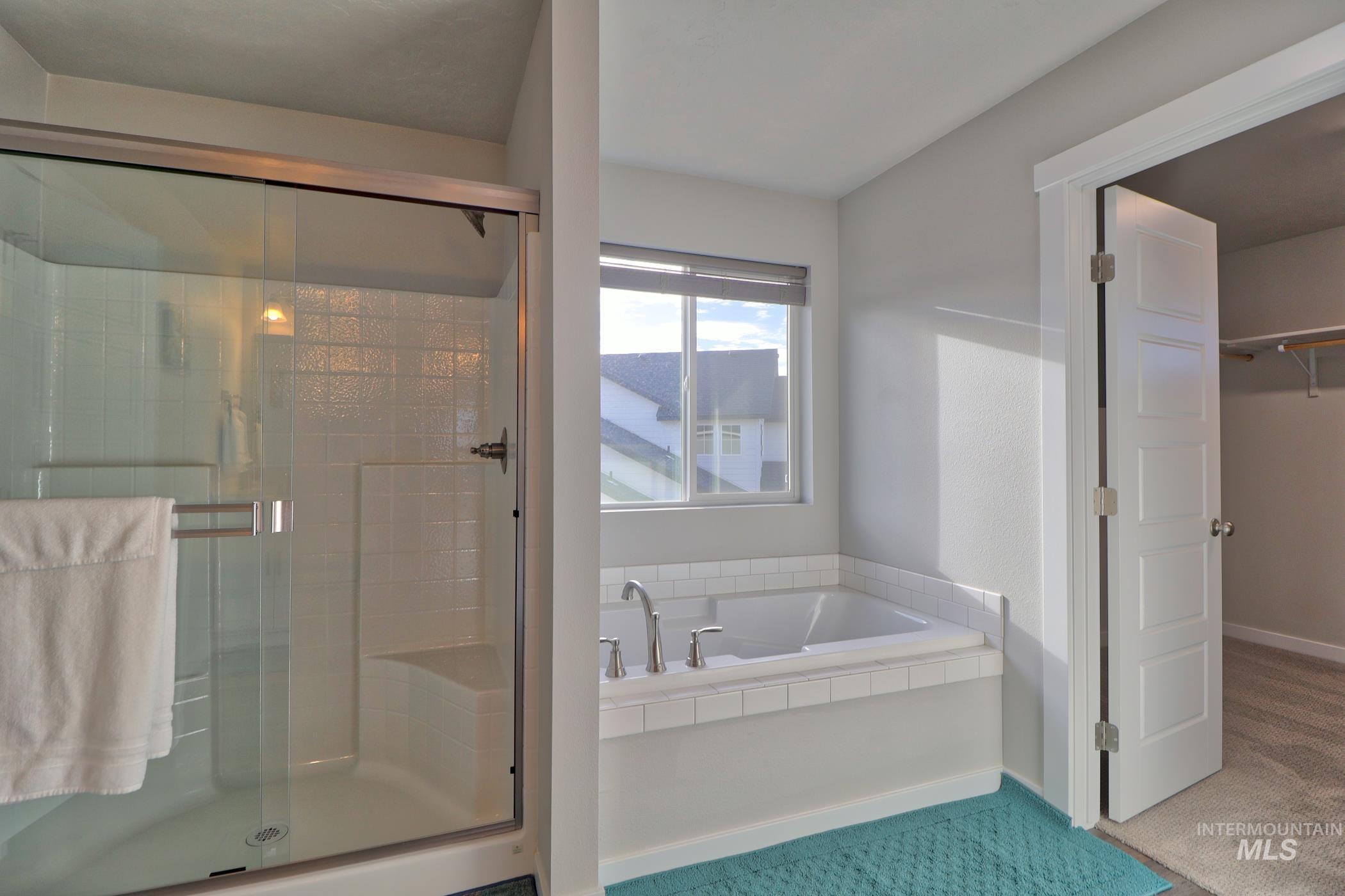 3508 South Edge Rim Way Meridian, ID 83642 - Photo 23 of 28 Bathroom with a glass-enclosed shower featuring a built-in bench, a separate soaking tub with tile surround, and a paneled door opening to a carpeted area