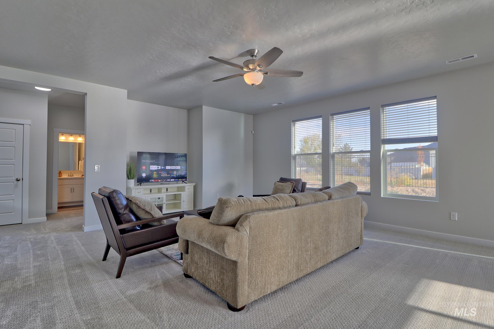 3508 South Edge Rim Way Meridian, ID 83642 - Photo 7 of 28 Carpeted living area featuring a ceiling fan with integrated lighting, three large windows with blinds, and light gray walls