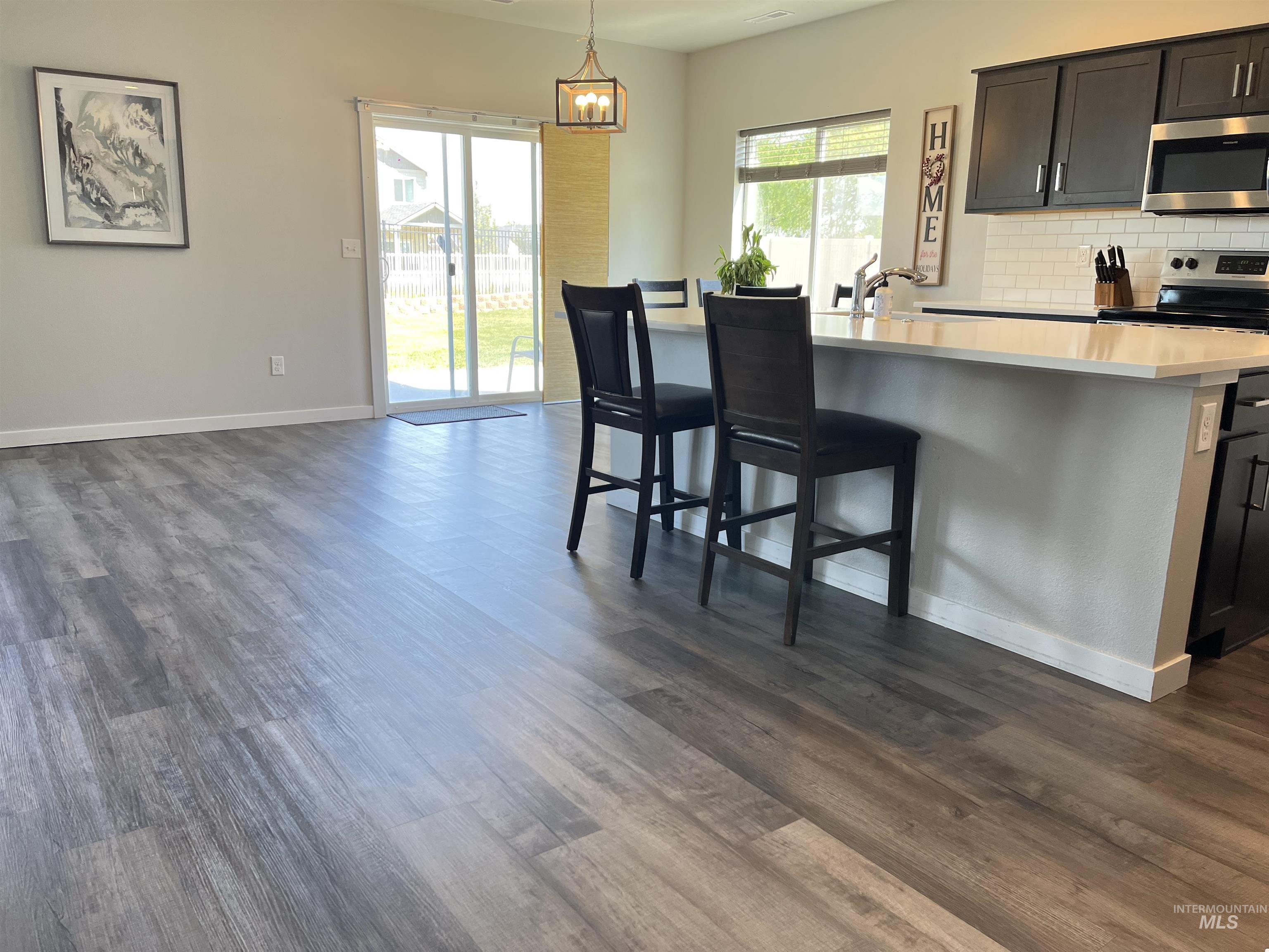 3508 South Edge Rim Way Meridian, ID 83642 - Photo 8 of 28 Open-concept living space featuring wood-finish flooring, a kitchen island with seating, dark shaker-style cabinetry, and a white subway tile backsplash