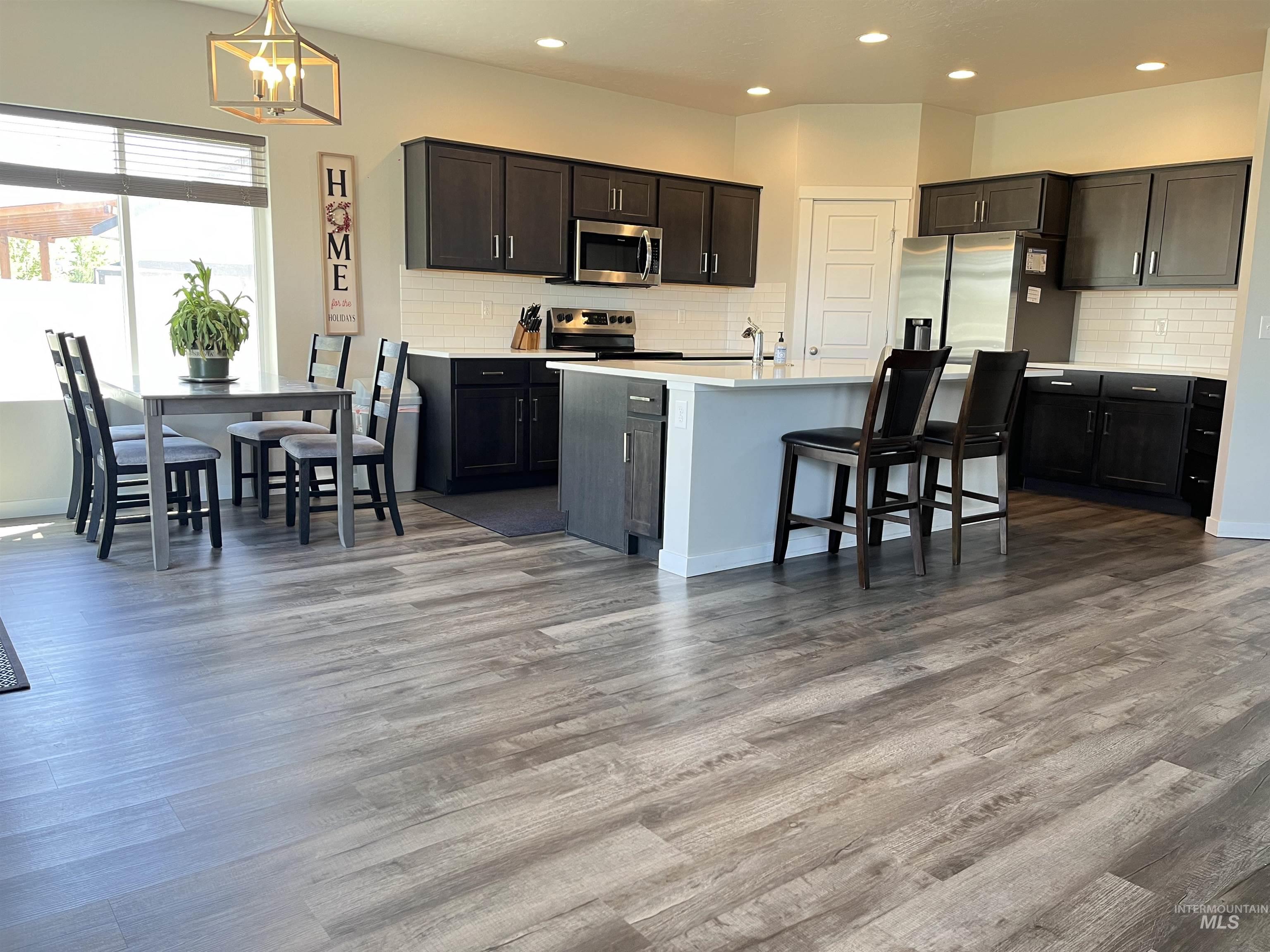 3508 South Edge Rim Way Meridian, ID 83642 - Photo 9 of 28 Open-concept kitchen featuring wood-finish flooring, dark wood cabinetry, white subway tile backsplash, a center island with countertop seating, and stainless steel appliances