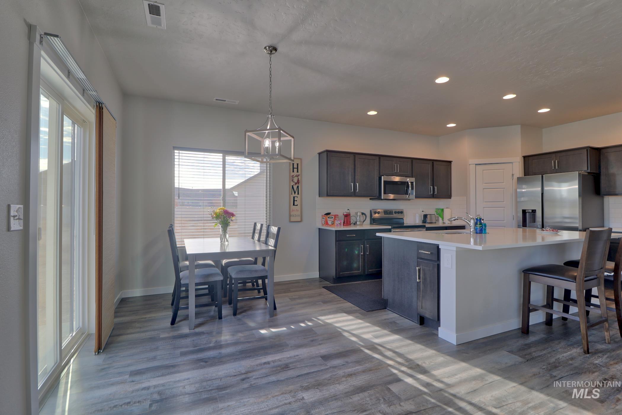 3508 South Edge Rim Way Meridian, ID 83642 - Photo 10 of 28 Open-concept kitchen and dining area featuring wood-finish flooring, dark wood cabinetry, stainless steel appliances, a center island with a light-toned countertop, and recessed lighting