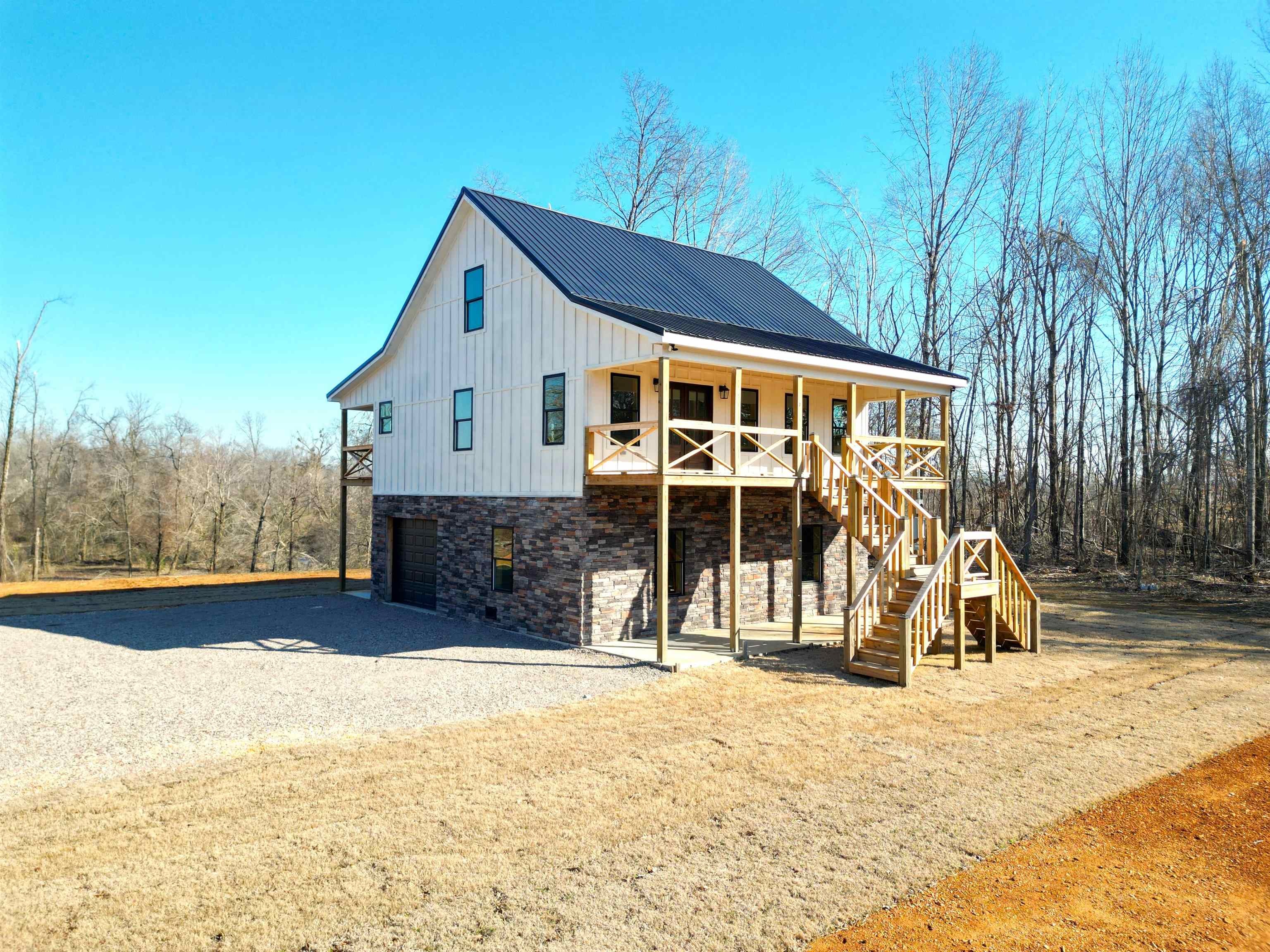 View of front facade with stone siding, an attached garage, gravel driveway, a metal roof, and board and batten siding