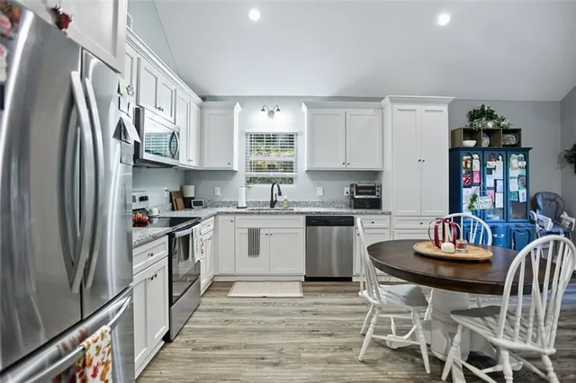 a kitchen with stainless steel appliances granite countertop a stove a sink dishwasher a refrigerator and white cabinets with wooden floor