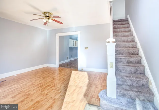 a view of an empty room with stairs and chandelier fan