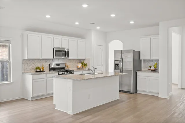 a kitchen with stainless steel appliances granite countertop a refrigerator a stove top oven a sink and dishwasher with wooden floor