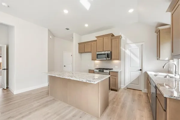 a large kitchen with stainless steel appliances granite countertop a stove a sink a refrigerator and white cabinets with wooden floor