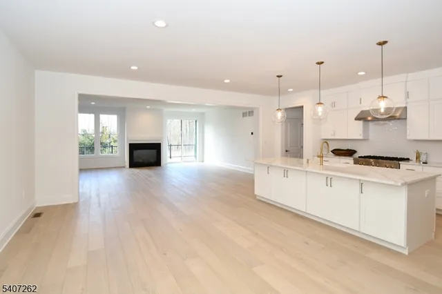 a large white kitchen with stainless steel appliances granite countertop a stove a sink a refrigerator and a dining table with wooden floor