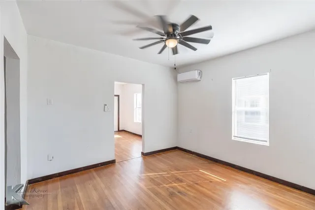 an empty room with wooden floor chandelier fan and windows
