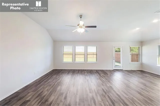 an empty room with wooden floor chandelier fan and windows