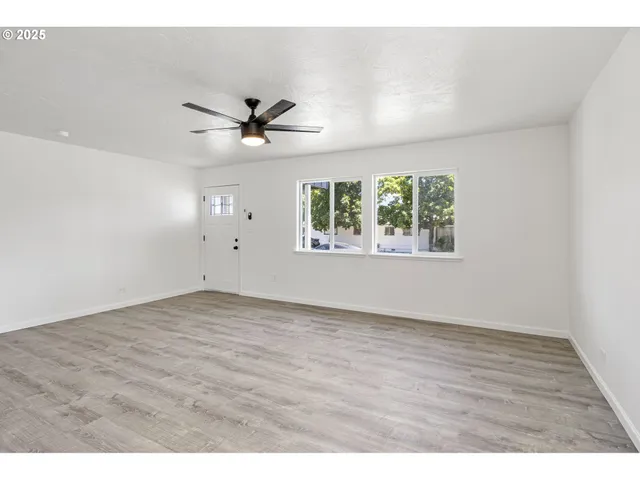 an empty room with wooden floor ceiling fan and windows