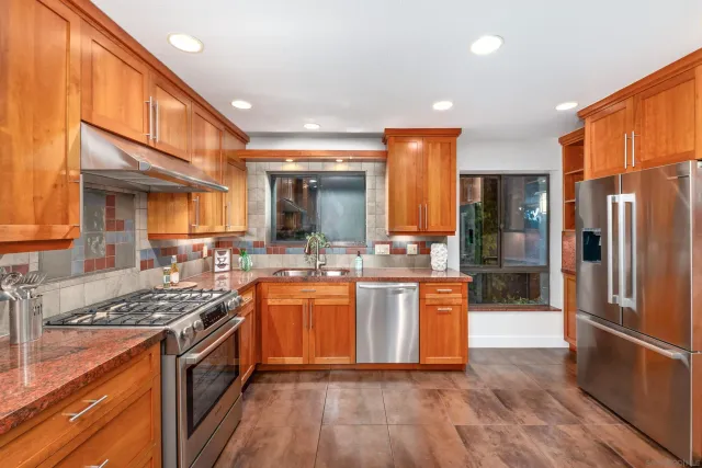 a kitchen with stainless steel appliances granite countertop a stove a sink dishwasher a refrigerator and white cabinets with wooden floor