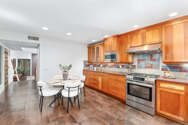 a kitchen with stainless steel appliances granite countertop a stove top oven a sink dishwasher a dining table and chairs with wooden floor