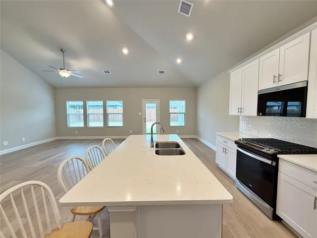 a kitchen with granite countertop a stove a sink a refrigerator and white cabinets with wooden floor