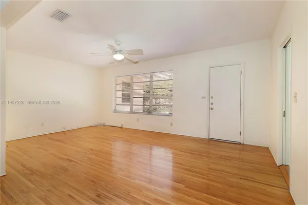 an empty room with wooden floor ceiling fan and windows