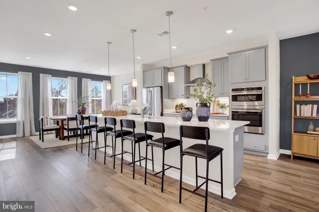 a kitchen with stainless steel appliances kitchen island granite countertop a dining table chairs and a refrigerator