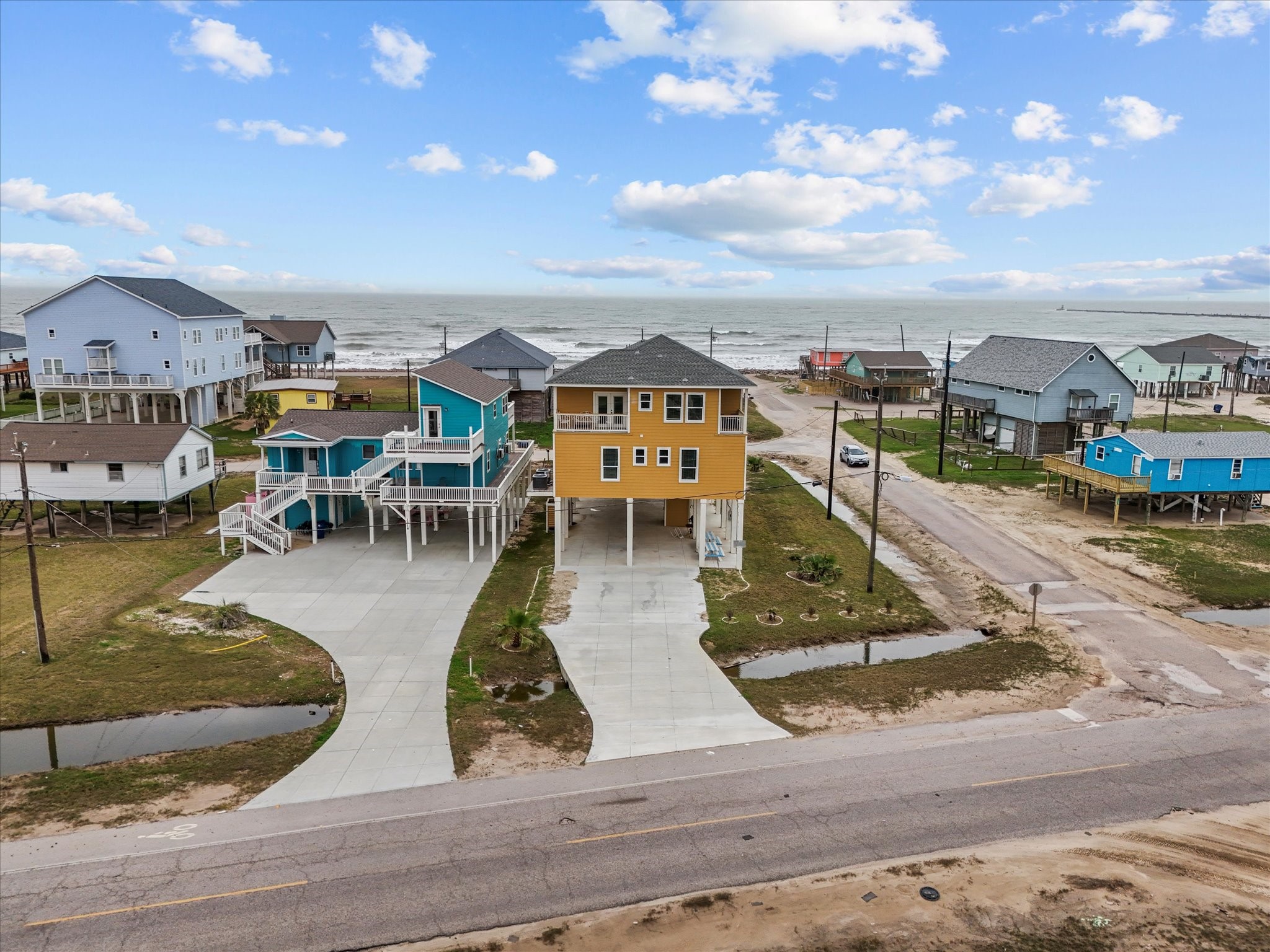 1018 Seashell Drive Surfside Beach, TX 77541 - Photo 6 of 49 This coastal property features a vibrant gold stilt house with a spacious driveway, offering picturesque ocean views. The neighborhood includes similar elevated homes, providing a beachside living experience with direct access to the shore. Ideal for those seeking a serene seaside retreat.