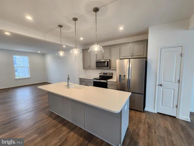 a large kitchen with stainless steel appliances a large kitchen island a refrigerator a stove and a wooden floors