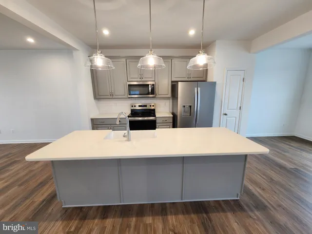 a large kitchen with kitchen island a sink dishwasher a refrigerator and a stove with wooden floor