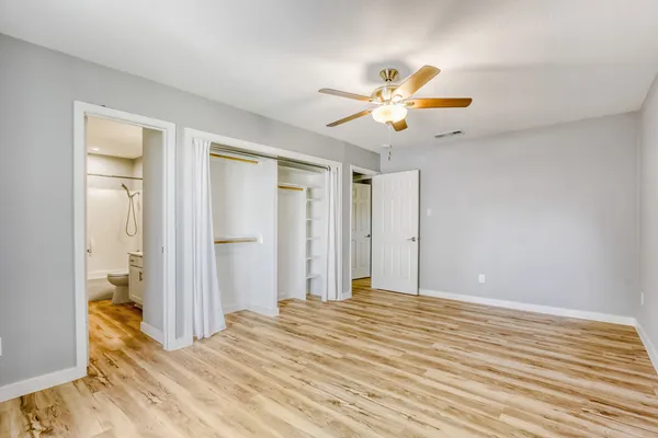 a view of an empty room with wooden floor and a ceiling fan