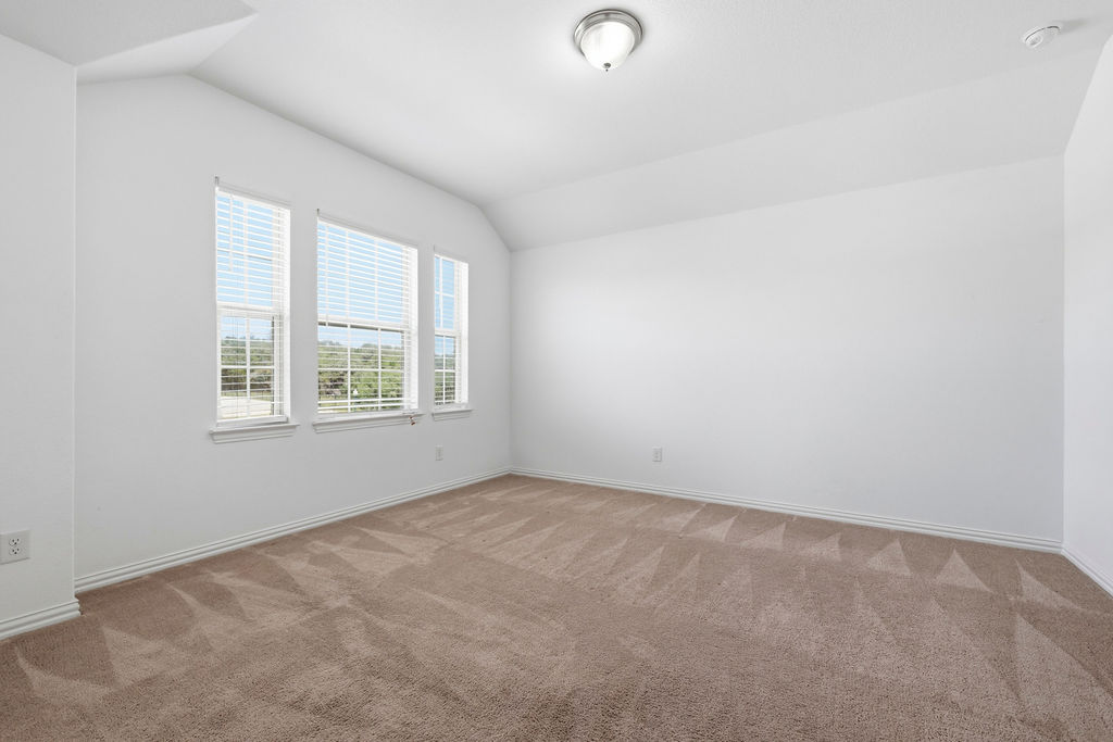 1005 Ridge Runner Drive Georgetown, TX 78628 - Photo 22 of 32 Carpeted room featuring three windows with blinds, a vaulted ceiling, and a flush mount ceiling light fixture