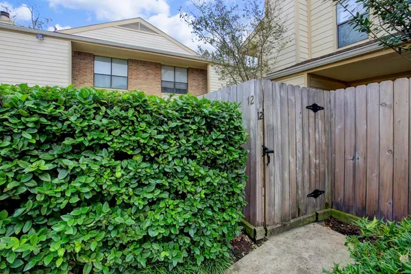 a view of a brick house with a small yard plants and a large tree