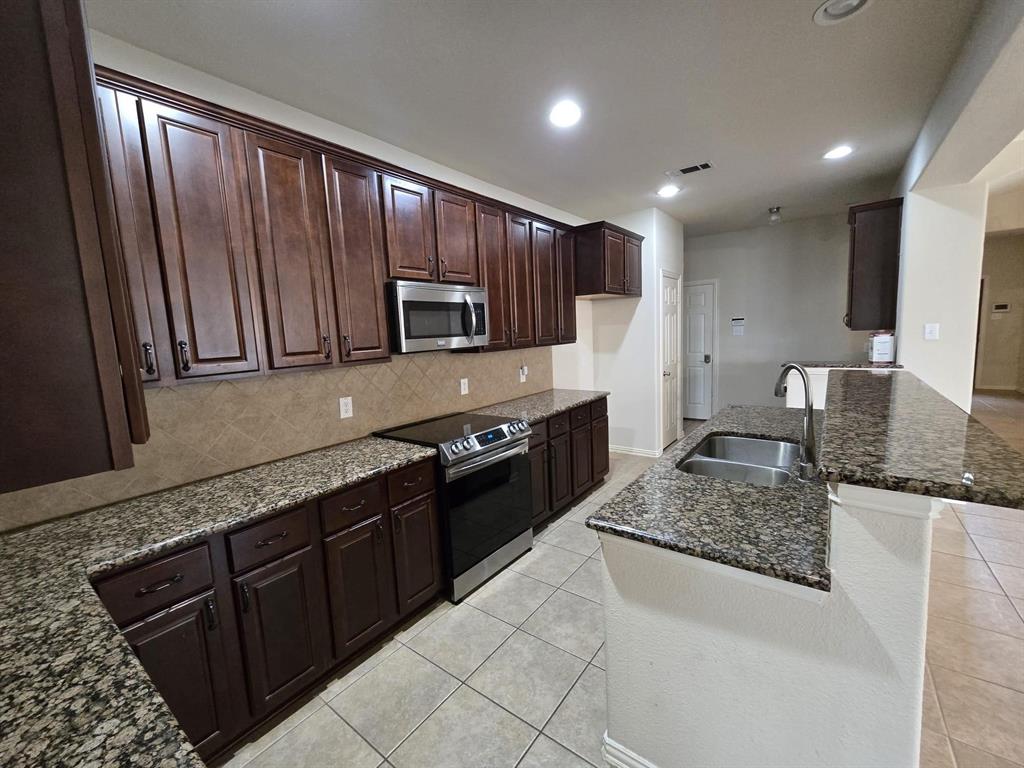 213 Willet Court Little Elm, TX 75068 - Photo 4 of 16 Kitchen with backsplash, dark stone countertops, sink, light tile patterned floors, and appliances with stainless steel finishes