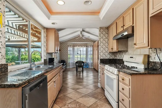 a kitchen with stainless steel appliances granite countertop a stove a sink and a granite counter tops with white cabinets next to a window
