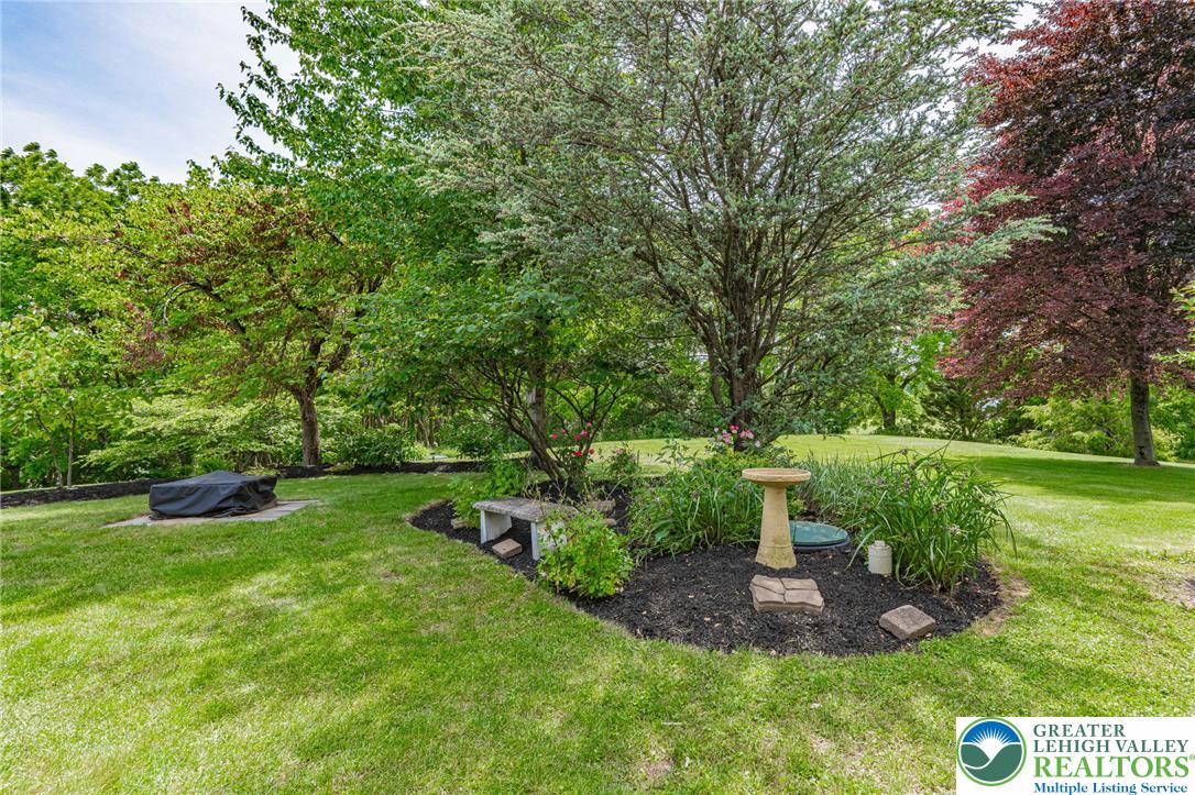 4542 Springfield Drive Coplay, PA 18037 - Photo 69 of 89 A verdant backyard with mature trees and landscaped garden beds, featuring a dedicated fire pit area for outdoor enjoyment.