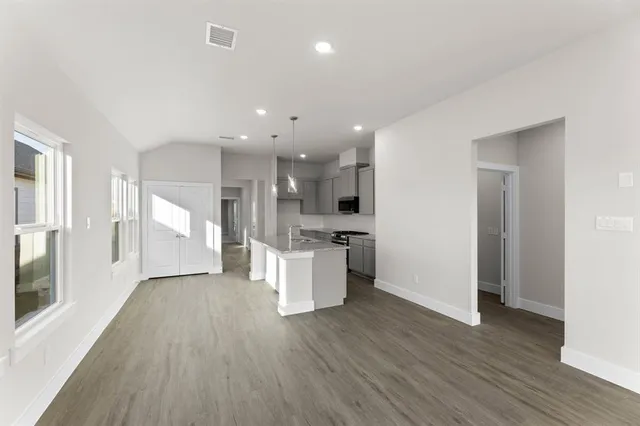 a view of an empty room and kitchen with wooden floor
