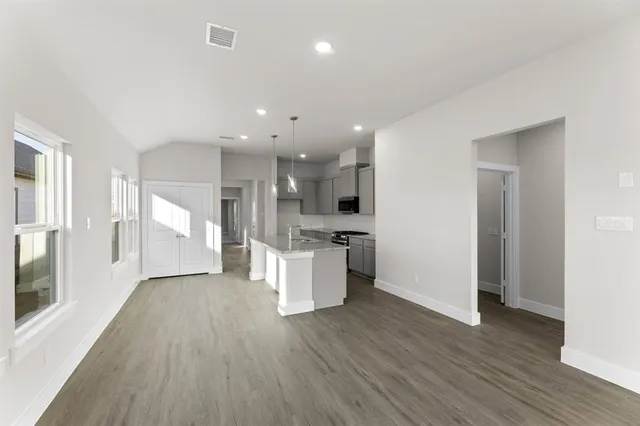 a view of an empty room and kitchen with wooden floor
