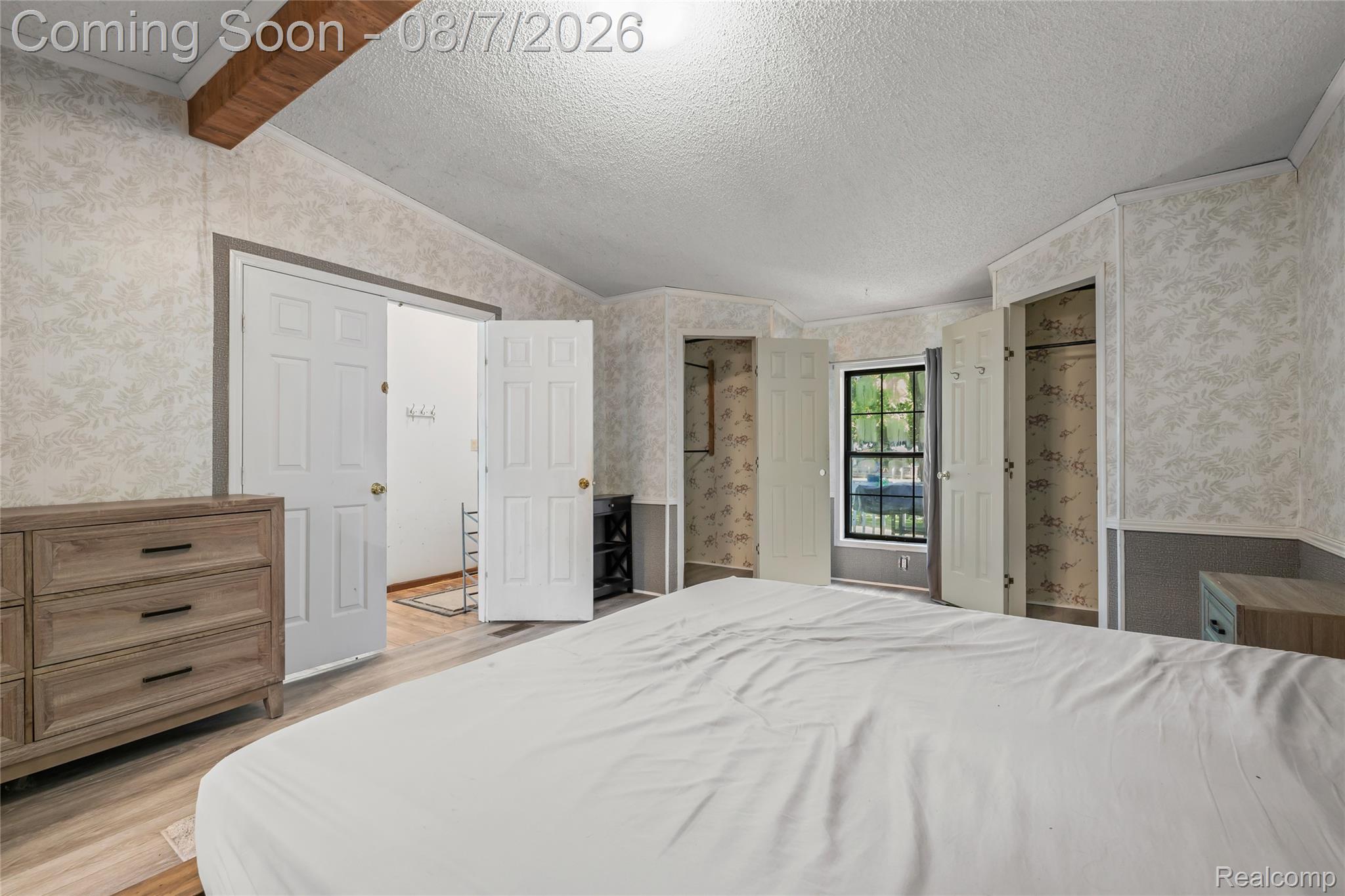 9940 Bunton Road Willis, MI 48191 - Photo 24 of 26 Room featuring wood-finish flooring, patterned wallpaper, a window with exterior views, and two closet areas with bi-fold doors
