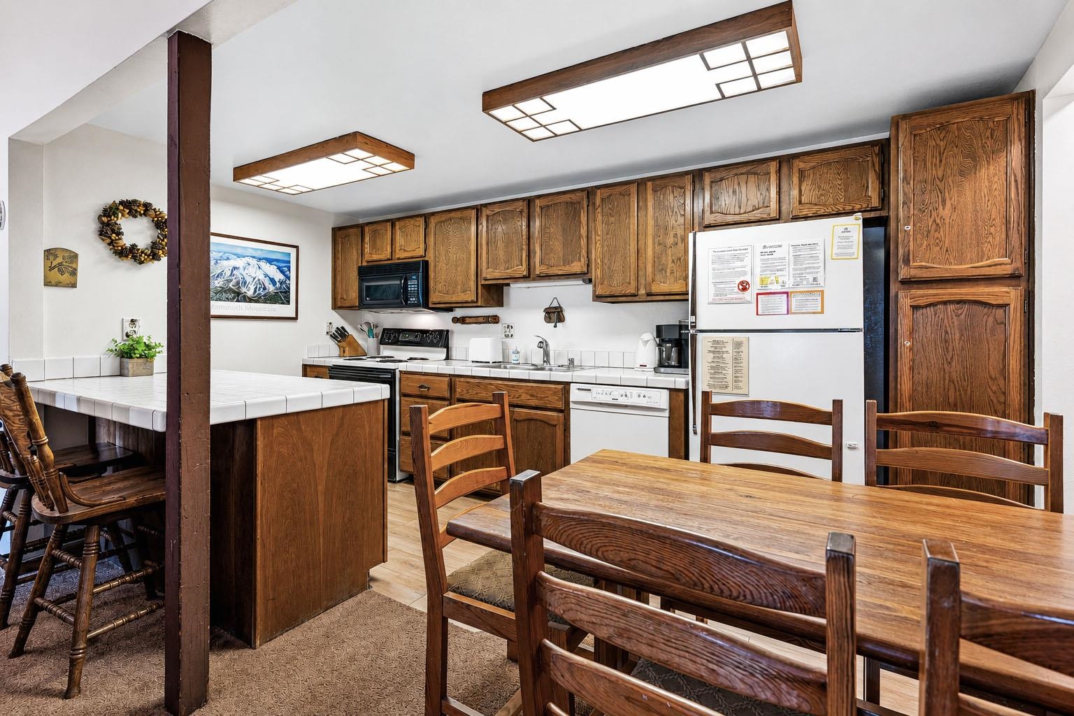 153 Lake Mary Road, Unit 114 Mammoth Lakes, CA 93546 - Photo 5 of 22 Kitchen featuring abundant wood-finish cabinetry, white tile countertops, and a full suite of appliances